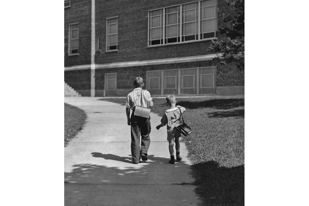 Pack-to-School-The-History-of-the-Backpack 1930s schoolchildren walk to school without backpacks. Boy on left with a satchel and the boy right carries an unwieldy bookstrap. Image via Getty Images.